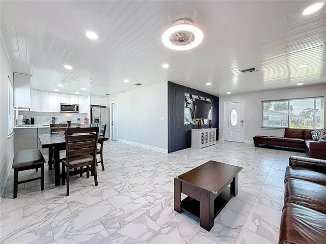 a kitchen with stainless steel appliances kitchen island granite countertop a dining table chairs and a refrigerator