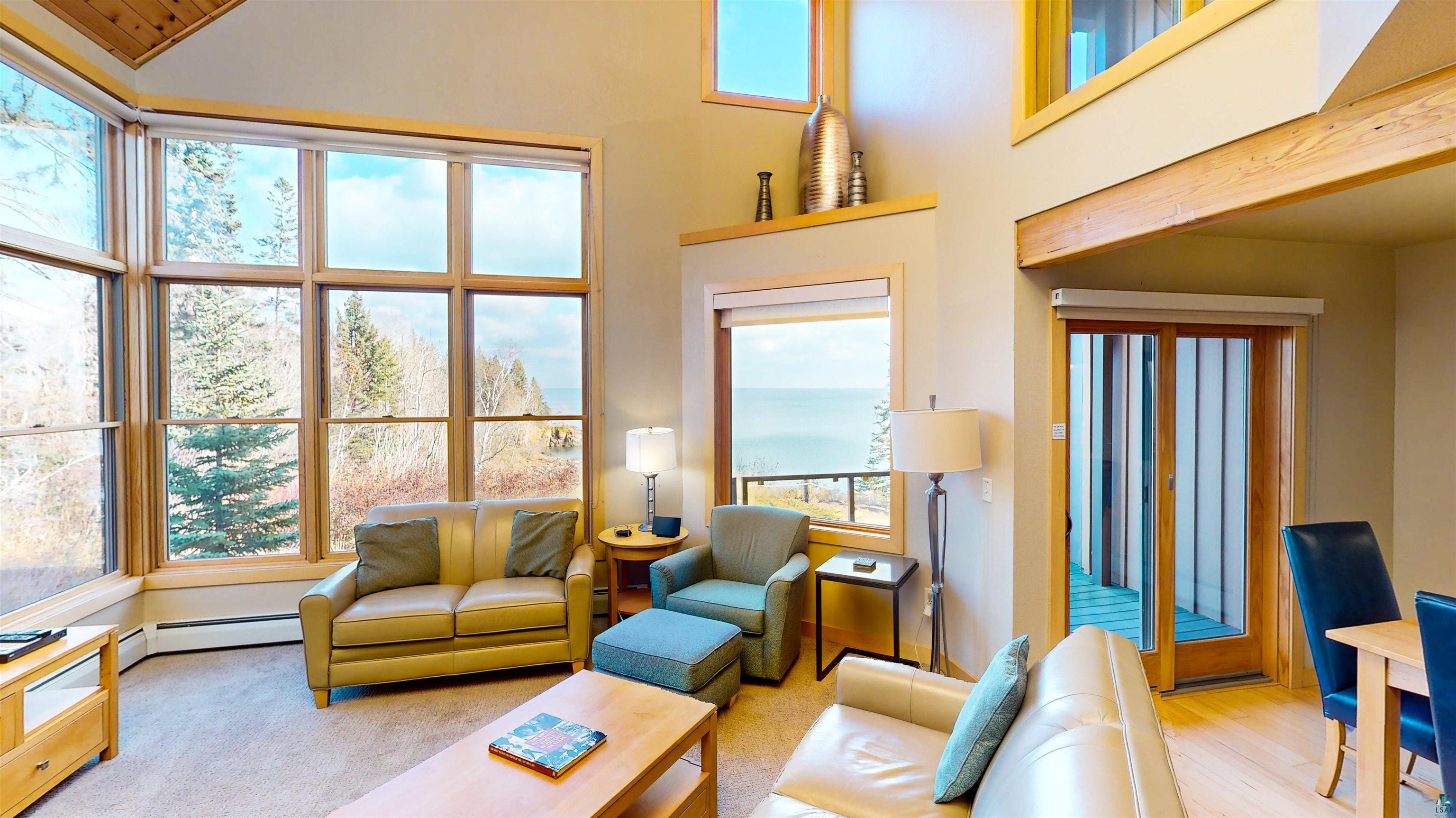 40 Surfside Drive, Unit 5D Tofte, MN 55615 - Photo 3 of 37 Spacious living area featuring expansive windows with natural wood frames, vaulted ceilings, light-toned wall finishes, wood-finish flooring, and a sliding glass door