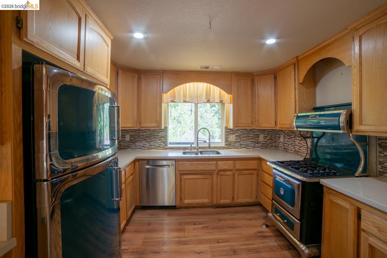 22401 Ridge Road Twain Harte, CA 95383 - Photo 13 of 52 Wood-finish flooring, light wood cabinetry, stone tile backsplash, white countertops, and stainless steel dishwasher