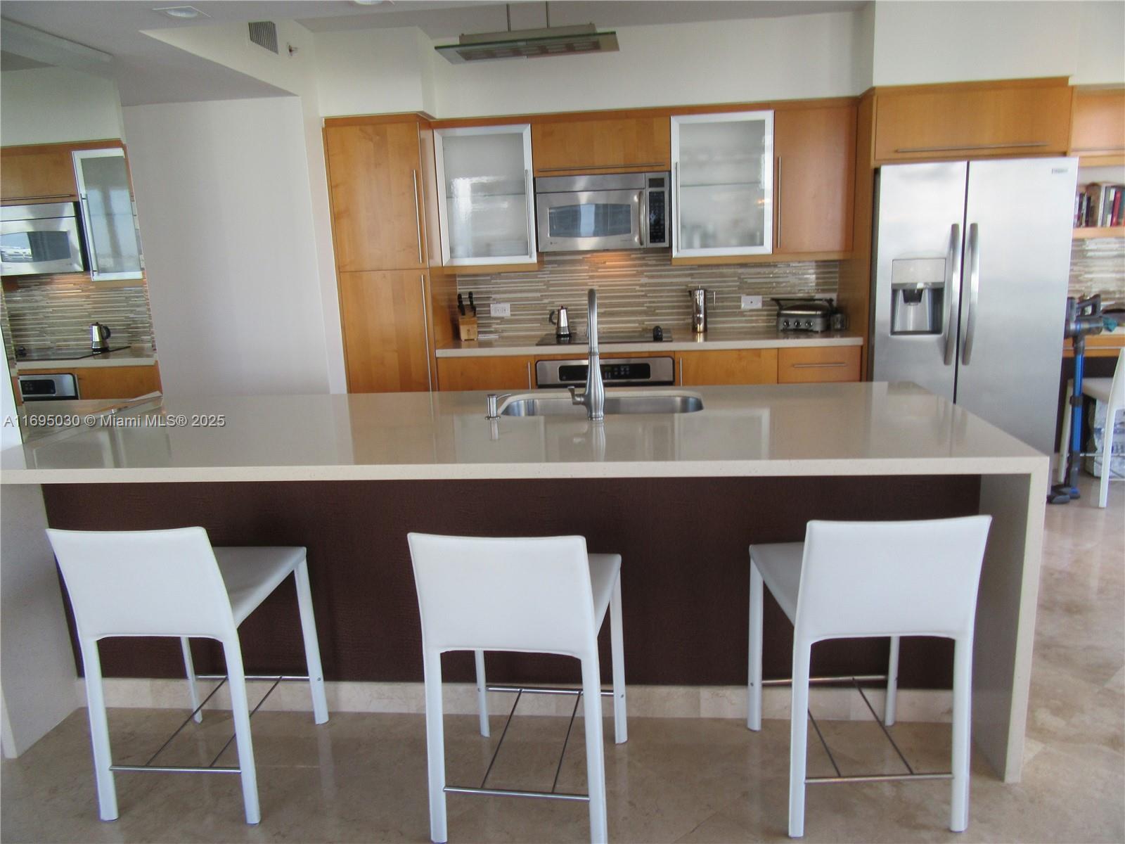 6365 Collins Avenue, Unit 1008 Miami Beach, FL 33141 - Photo 17 of 49 a dining room with stainless steel appliances kitchen island granite countertop a table chairs and a refrigerator