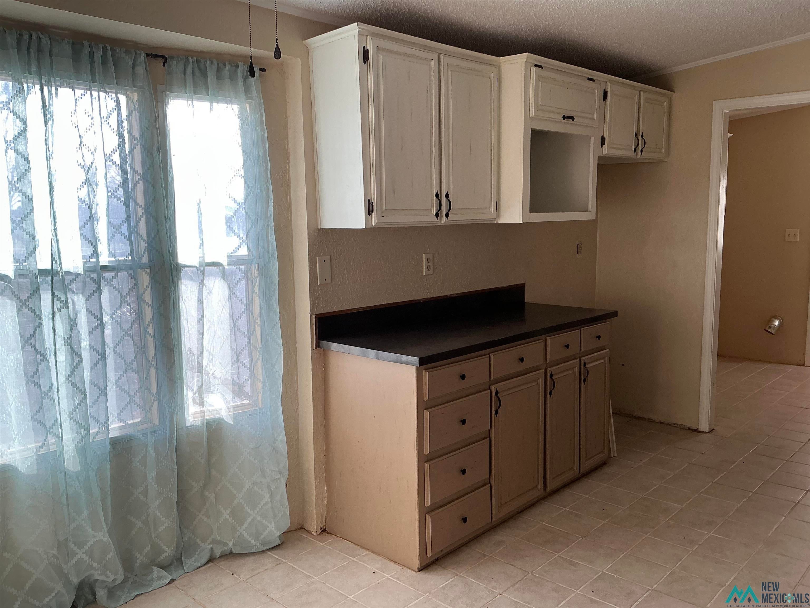 1020 South Fork Road Clovis, NM 88101 - Photo 14 of 37 Kitchen with dark countertops, a textured ceiling, light tile patterned floors, white cabinetry, and ornamental molding