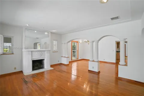 a view of an empty room with wooden floor fireplace and a window