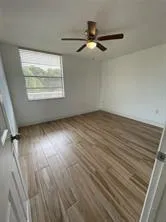 an empty room with wooden floor fan and windows