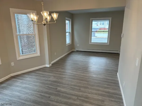 an empty room with wooden floor chandelier and windows