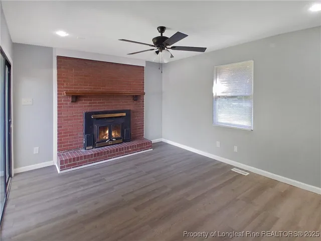 a view of an empty room with wooden floor fireplace and a window