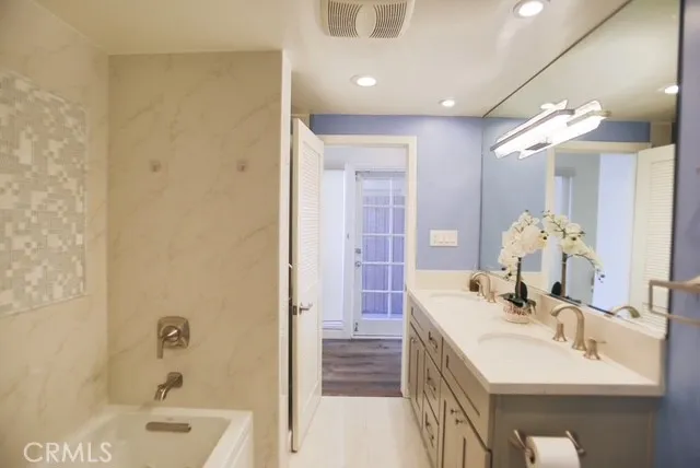 a bathroom with a double vanity sink a large mirror and a bathtub