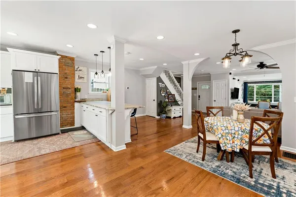 a kitchen with stainless steel appliances kitchen island granite countertop a refrigerator a stove a dining table and chairs with wooden floor