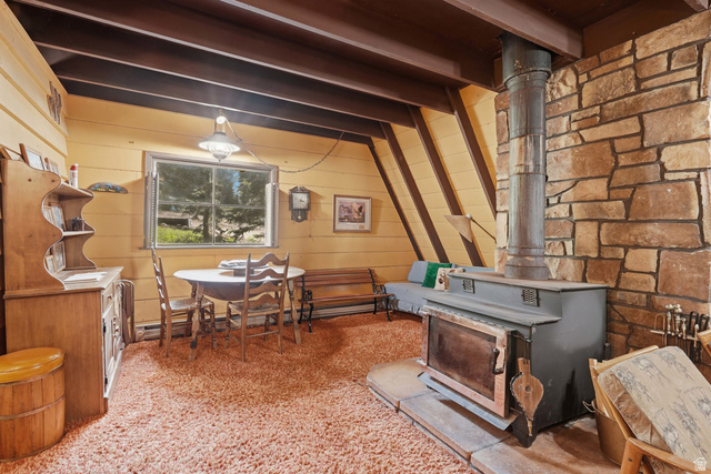 8505 South Snake Crk Road Salt Lake City, UT 84121 - Photo 9 of 67 A-frame interior featuring a stone accent wall with a built-in wood-burning stove, exposed wood ceiling beams, and horizontal wood paneling