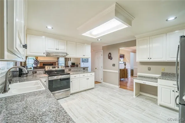 a kitchen with stainless steel appliances granite countertop a stove top oven a sink a refrigerator and white cabinets with wooden floor