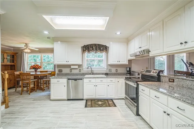 a kitchen with stainless steel appliances granite countertop a stove a sink dishwasher and white cabinets with wooden floor