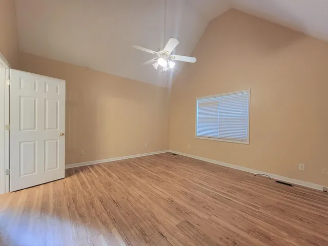 a view of an empty room with wooden floor and a ceiling fan
