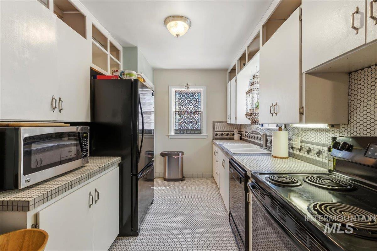 4619 Freemont Street Boise, ID 83706 - Photo 7 of 27 Galley kitchen featuring white cabinetry, black appliances, hexagon tile flooring, patterned tile backsplash, and a decorative window