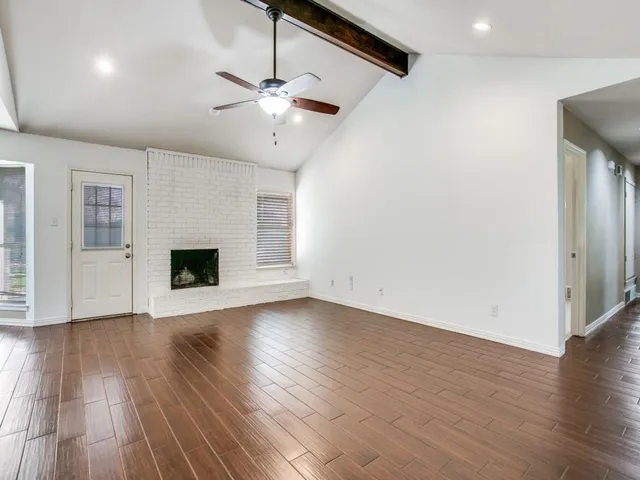 an empty room with wooden floor fireplace and windows