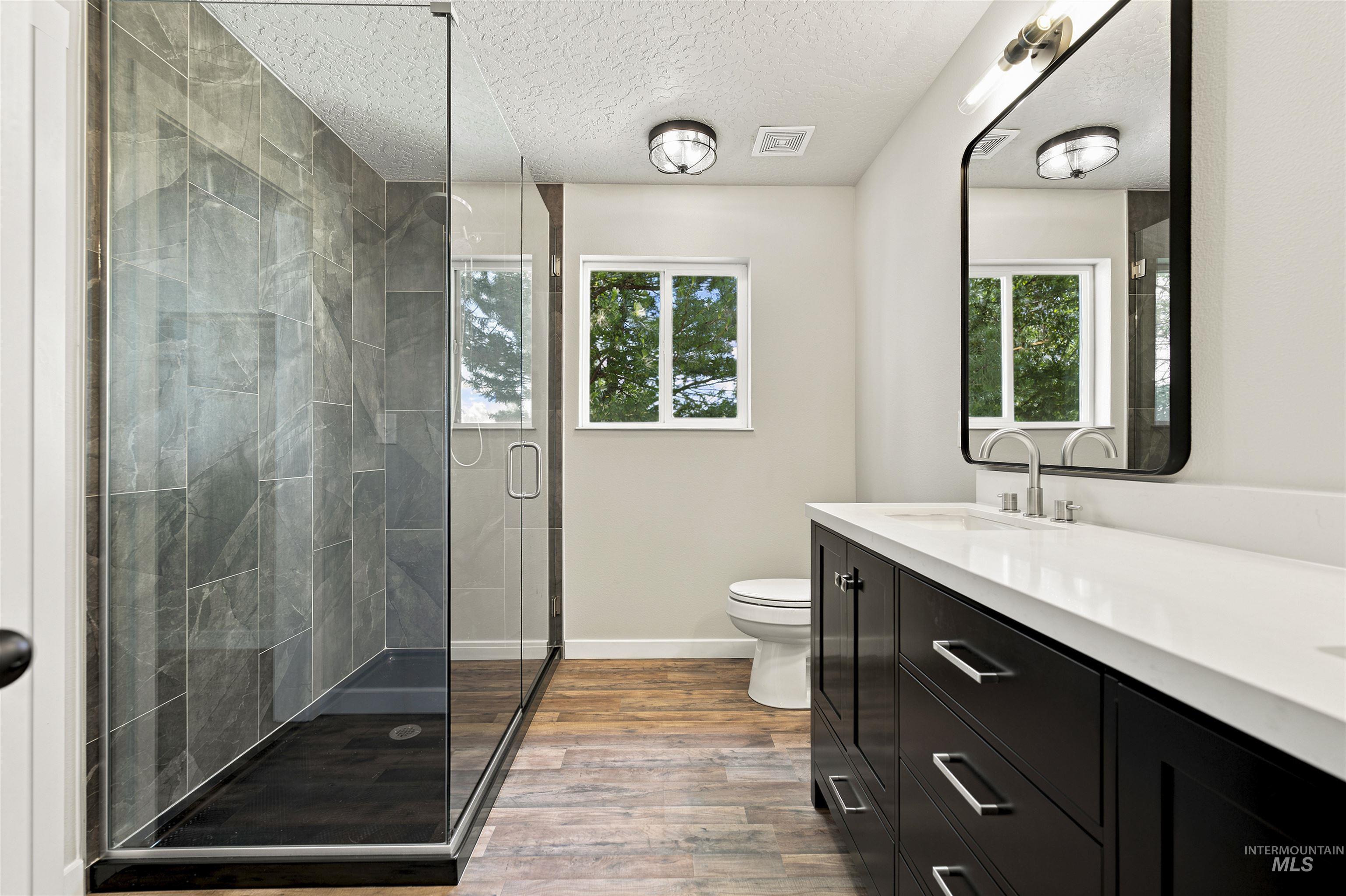 24864 Coventry Drive Caldwell, ID 83607 - Photo 26 of 49 Modern bathroom featuring a frameless glass shower enclosure with large format grey tile, a dark wood-finish double vanity with a white countertop, and wood-finish flooring