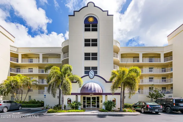 a front view of a building with lot of cars and trees