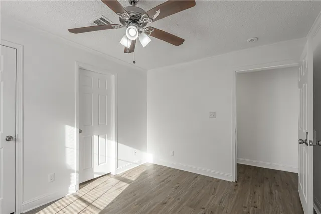 an empty room with wooden floor fan and windows