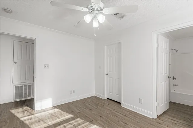 a view of an empty room with wooden floor and a ceiling fan
