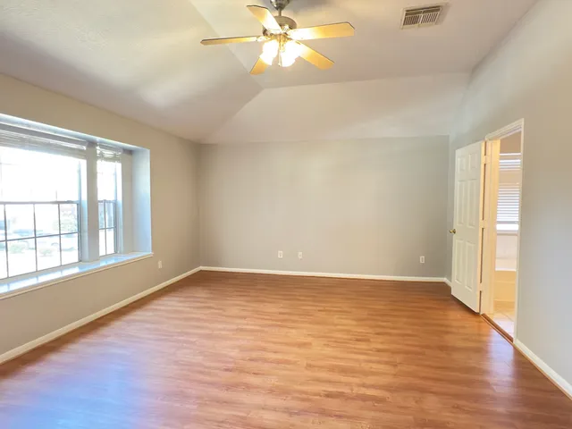 an empty room with wooden floor fan and windows