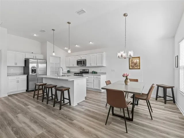 a kitchen with stainless steel appliances kitchen island granite countertop a dining table chairs and white cabinets
