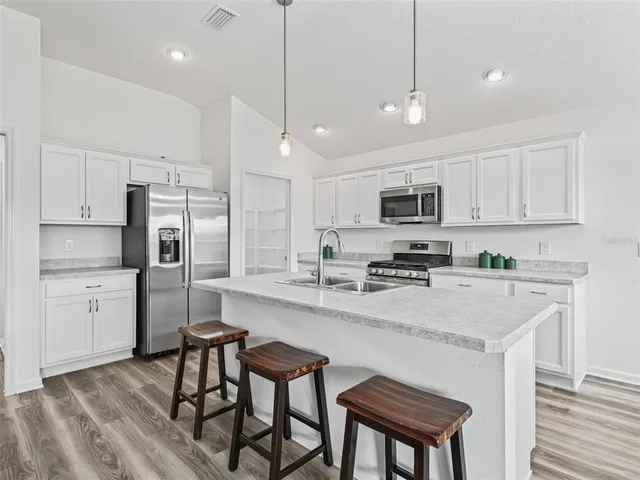 a kitchen with stainless steel appliances granite countertop a stove top oven a refrigerator a sink and white cabinets