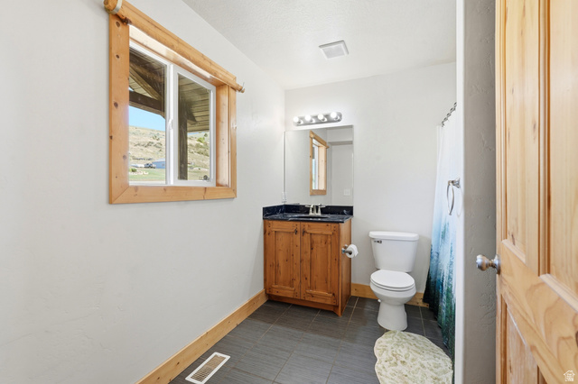 306 Spring Road Preston, ID 83263 - Photo 24 of 55 Bathroom featuring a wood-framed window, natural wood vanity with dark countertop, white toilet, and gray tile flooring