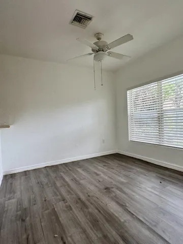 an empty room with wooden floor fan and windows