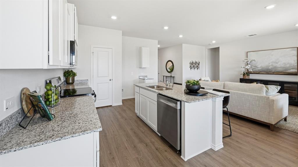 1957 Freeman Street Tyler, TX 75704 - Photo 8 of 25 Open-concept kitchen featuring white cabinetry, granite-finish countertops, stainless steel appliances, a central island with a double sink, and wood-finish flooring