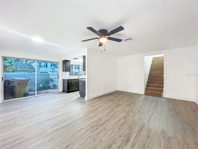 an empty room with wooden floor ceiling fan and windows