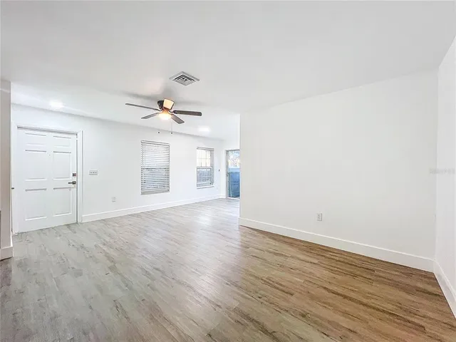 a view of an empty room with wooden floor and a ceiling fan