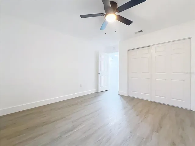 an empty room with wooden floor ceiling fan and windows