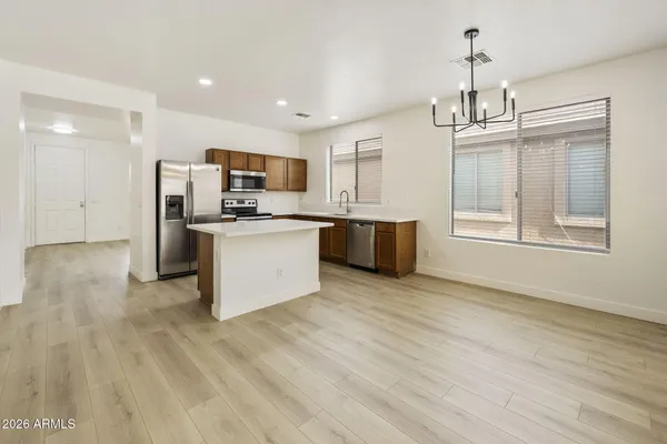 a kitchen with stainless steel appliances granite countertop a stove top oven a sink dishwasher a refrigerator and a dining table with wooden floor