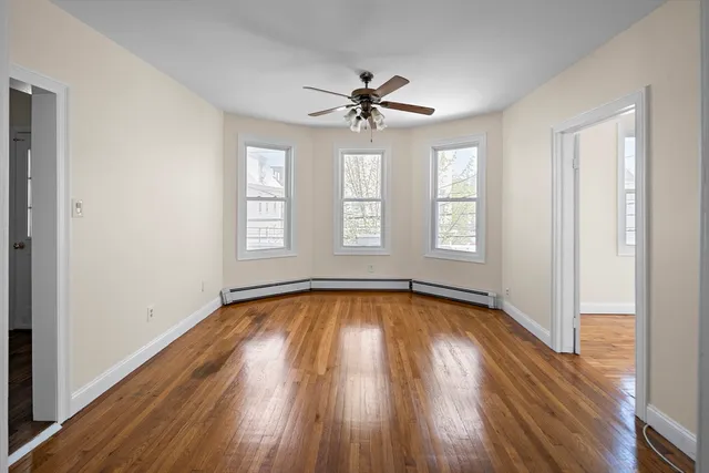 an empty room with wooden floor chandelier fan and windows