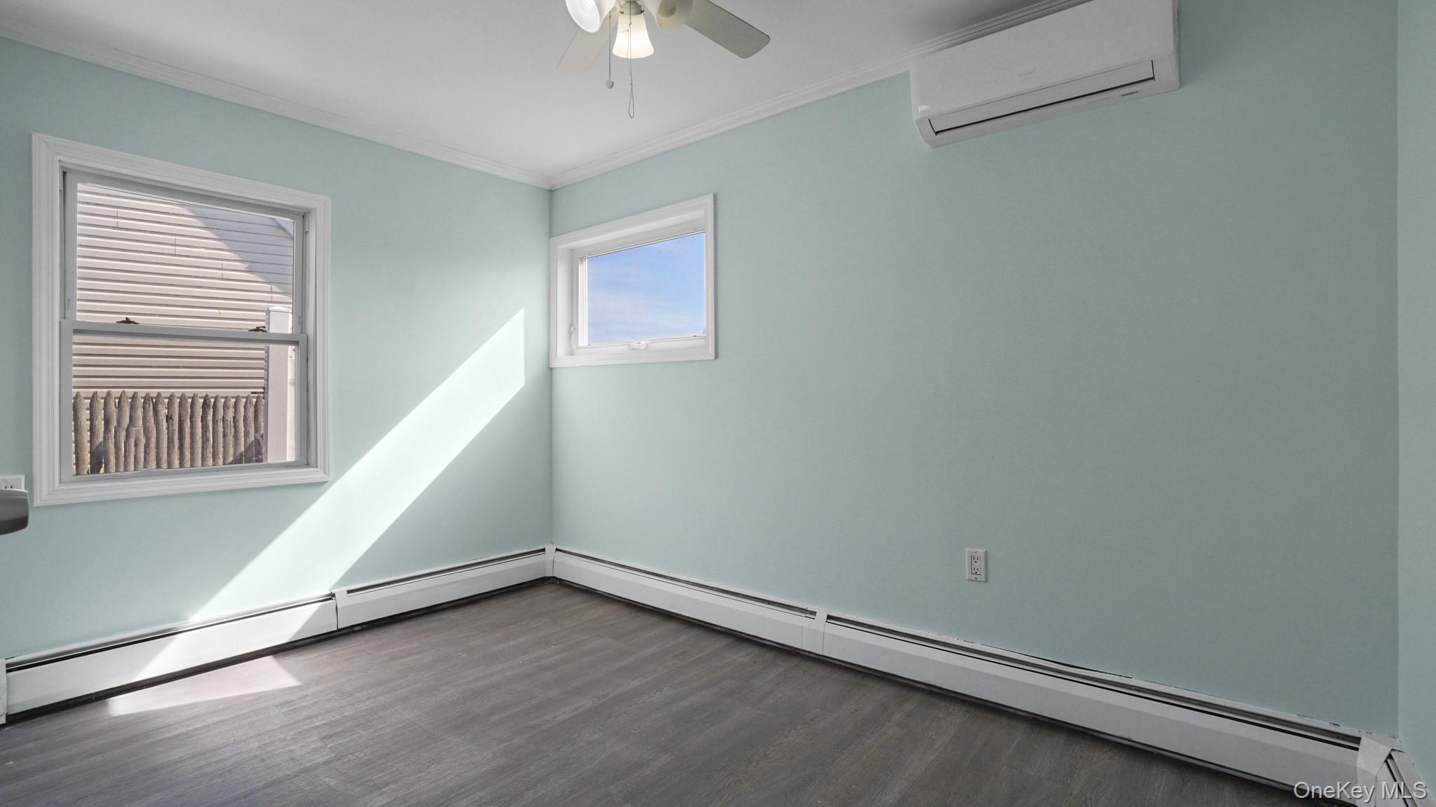 63 Blacksmith Road Levittown, NY 11756 - Photo 16 of 25 Interior space featuring light blue walls, wood-finish flooring, two windows with white trim, a ceiling fan, and a wall-mounted climate control unit