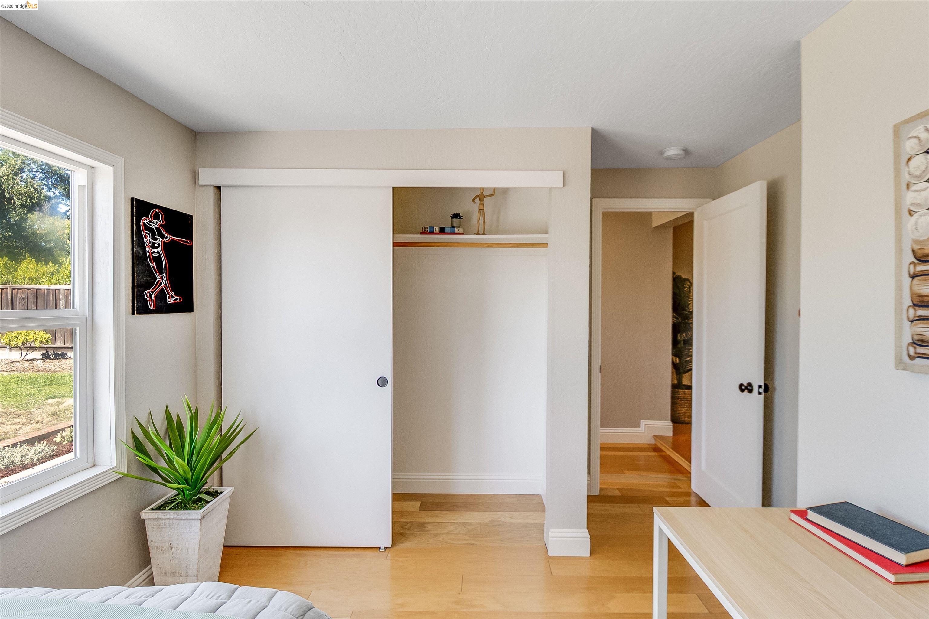 346 Valley View Road Pleasant Hill, CA 94523 - Photo 35 of 57 Bedroom featuring a large window, light wood-finish flooring, a white sliding barn door closet, an interior doorway, and neutral wall tones