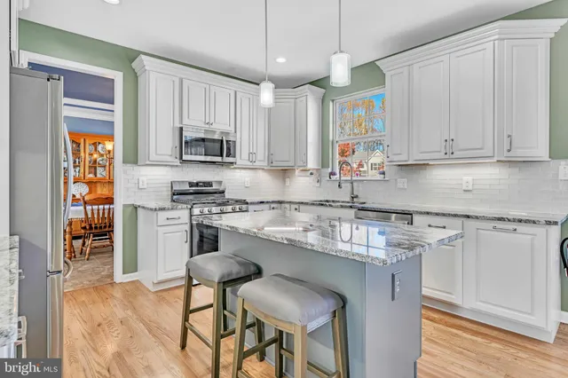 a kitchen with stainless steel appliances granite countertop a stove top oven a refrigerator a sink and white cabinets with wooden floor