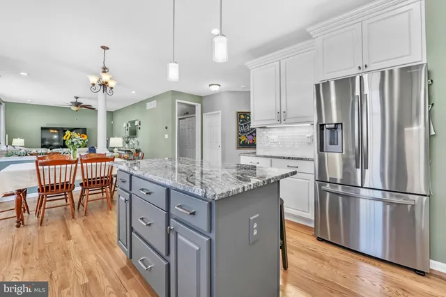 a kitchen with granite countertop a refrigerator a stove a kitchen island with furniture and wooden floor