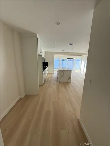 a view of an empty room with wooden floor and a hallway