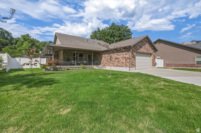689 Apple Drive Logan, UT 84321 - Photo 3 of 52 Brick and stone exterior residence featuring an attached garage, covered front porch, and a white privacy fence enclosing the side yard
