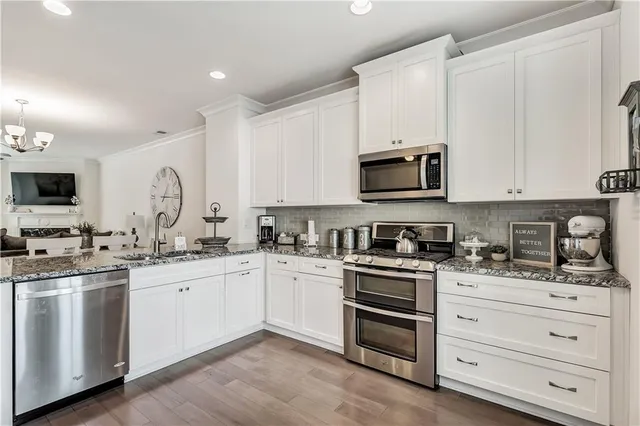 a kitchen with stainless steel appliances a sink dishwasher a refrigerator and white cabinets with wooden floor