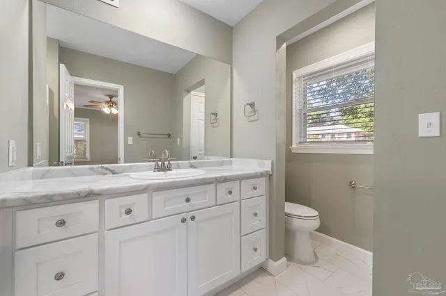 a bathroom with a granite countertop toilet a sink a mirror and a window