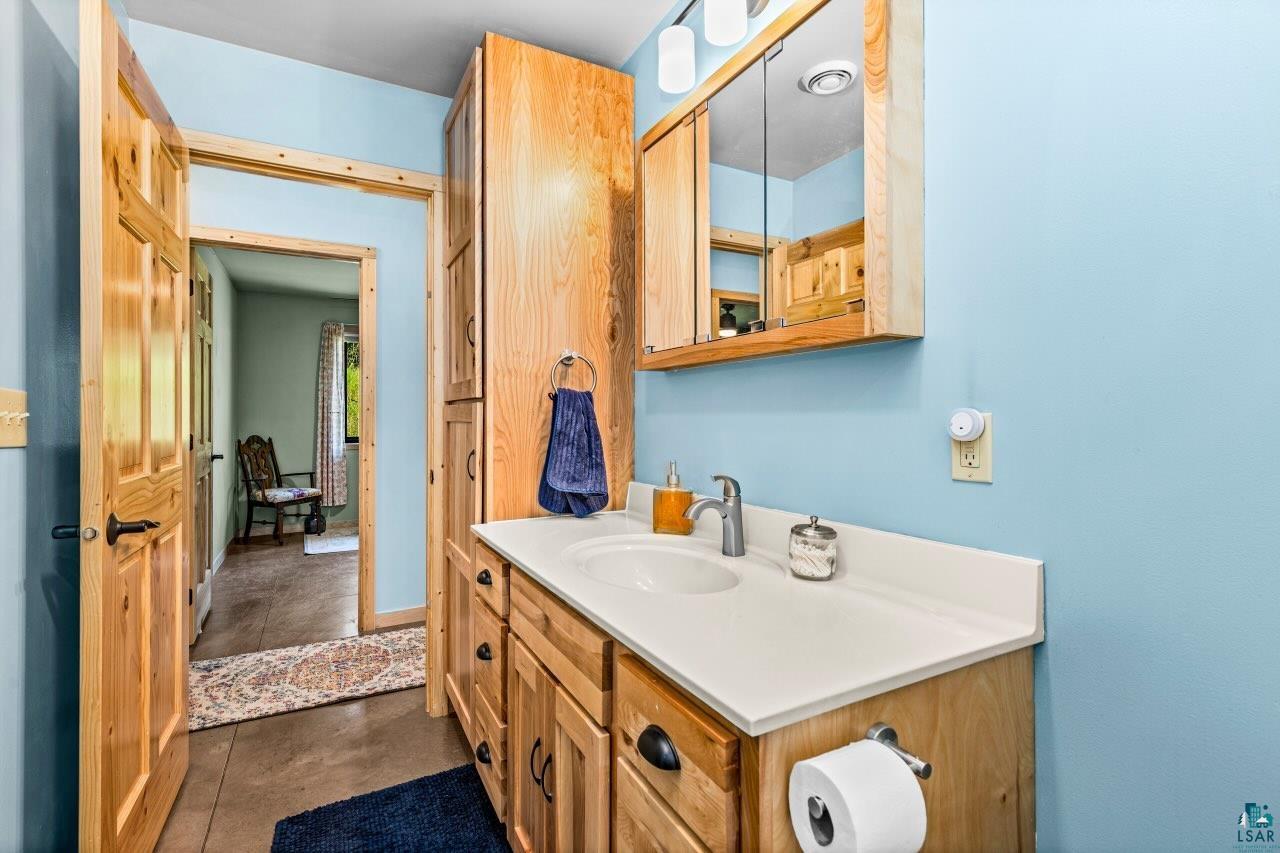 265 Mink Ranch Road Lutsen, MN 55612 - Photo 18 of 33 Bathroom featuring a single vanity with a white countertop and wood-finish cabinetry