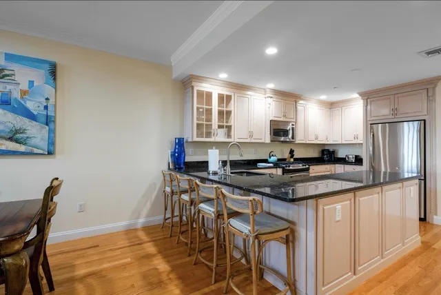 a kitchen with stainless steel appliances granite countertop a stove a sink a refrigerator white cabinets and chairs