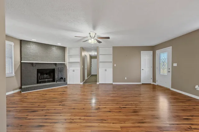 a view of an empty room with wooden floor fireplace and a window