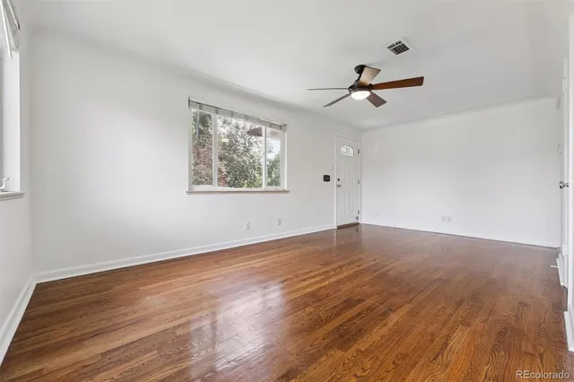 an empty room with wooden floor ceiling fan and windows