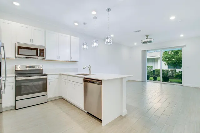 a large white kitchen with kitchen island a sink a center island stainless steel appliances and a refrigerator