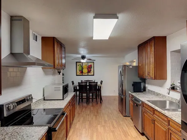 a kitchen with stainless steel appliances granite countertop a stove top oven a sink a dining table and chairs with wooden floor