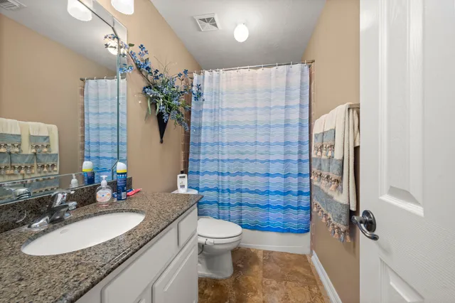 a bathroom with a granite countertop sink a toilet a mirror a vanity and shower