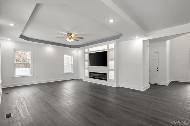 a view of a livingroom with wooden floor a ceiling fan and windows
