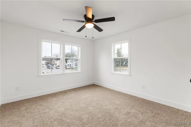 an empty room with ceiling fan and windows