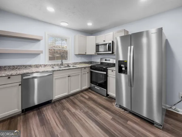 a kitchen with stainless steel appliances granite countertop a refrigerator a sink dishwasher a stove top oven a refrigerator and white cabinets with wooden floor